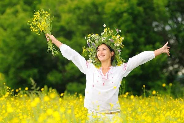 Jonge glimlachende vrouw staande en met gele bloemen in de wei — Stockfoto