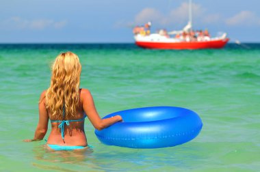 Bikinili genç bir kadın yüzme çemberiyle deniz suyunda ters duruyor.