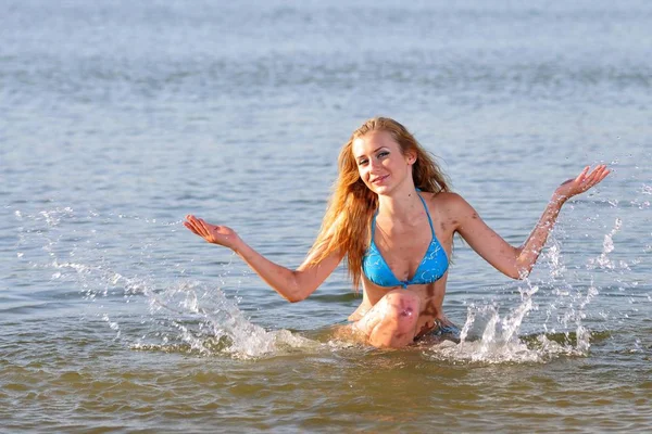 Mujer joven en bikini parada en el agua y haciendo olas —  Fotos de Stock