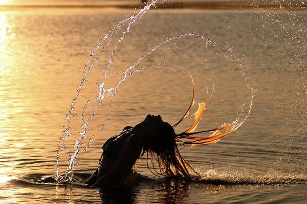 Silhuett av kvinna som står i vatten och gör vatten cirklar med hår — Stockfoto