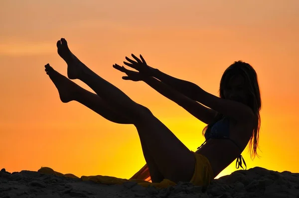 Silhouette di donna magra seduta con le gambe sollevate al tramonto — Foto Stock