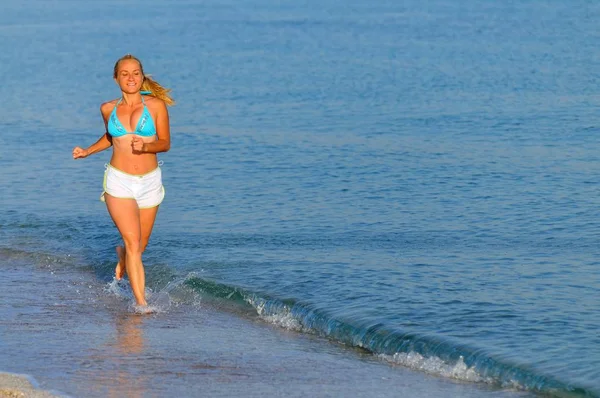 Mujer joven en ropa deportiva corriendo cerca de todavía borde del mar y sonriendo — Foto de Stock