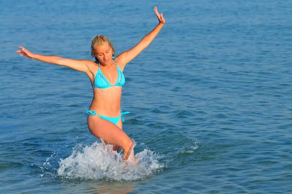 Spor giyimli genç bir kadın deniz kenarında koşuyor ve gülümsüyor. — Stok fotoğraf
