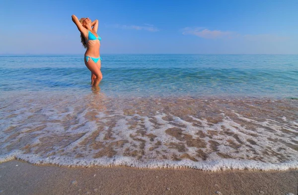 Jovem loira de biquíni azul em pé em água do mar e desfrutando do sol — Fotografia de Stock