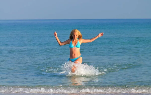 Mladá žena ve sportovním oblečení běží v blízkosti klidné mořské hrany a usmívá — Stock fotografie
