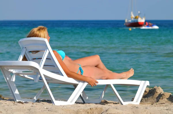 Junge Frau im Bikini liegt auf Sonnenliege am stillen Meerwasserrand und genießt Sonne — Stockfoto