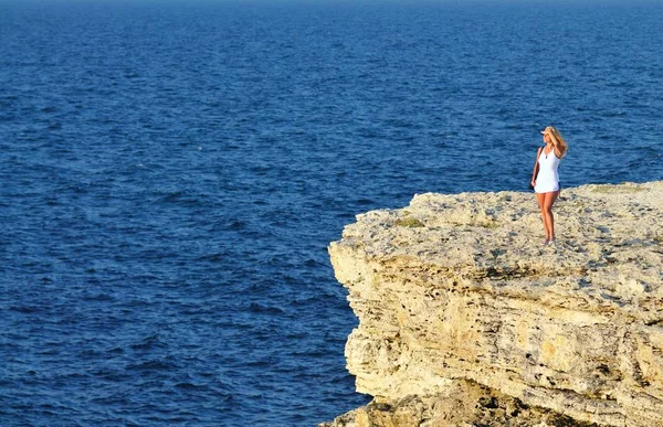 Young woman standing on rock over sea water and looking at horizon — Stock Photo, Image