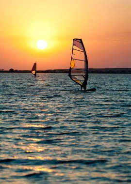 Still sea surface, man practicing wind surfing and golden sunset in sky clipart