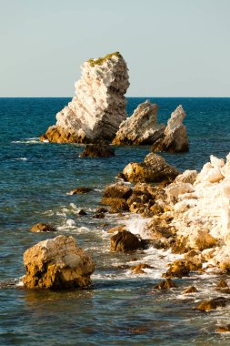 Durgun mavi deniz suları kıyıları, kayalık kıyı şeridi ve parlak güneş.