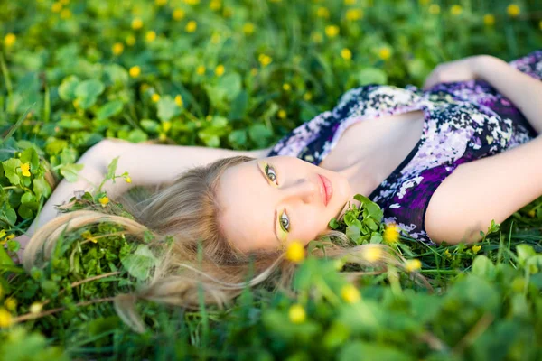 Portré fiatal gyönyörű szőke nő feküdt a fű és a virágok a nyári napon a zöld természet táj — Stock Fotó