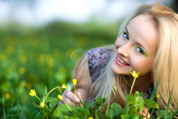 Portrét mladé krásné blondýny ležící v trávě a květiny v letní den se zelenou přírodou krajiny — Stock fotografie
