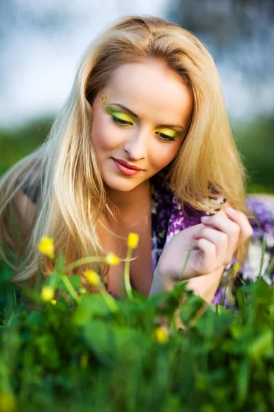 Portrait of young beautiful blond woman lying in grass and flowers on summer day with green nature landscape — Stock Photo, Image