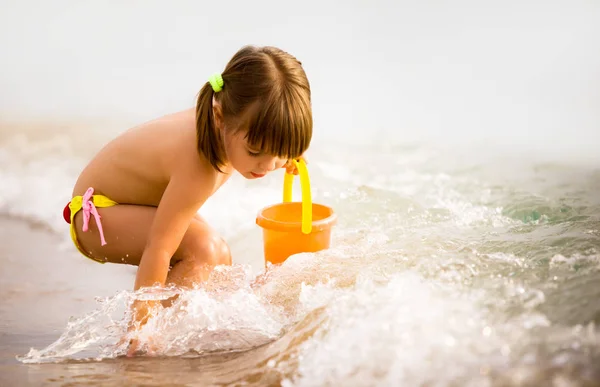 Niña jugando con juguetes en el borde del agua de mar — Foto de Stock