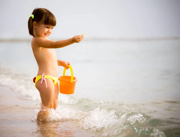 Piccola ragazza che gioca con i giocattoli nel bordo dell'acqua di mare — Foto Stock