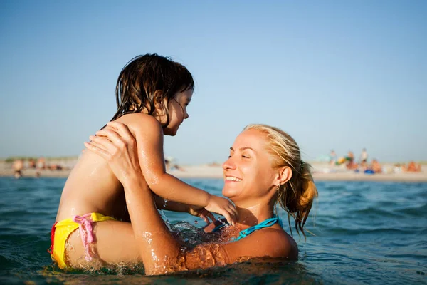 Young mother standing in water and helping to swim her small daughter — Stock Photo, Image