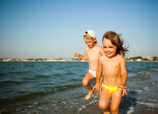 Happy little girl and boy running on water edge in sunshine — Stock Photo, Image