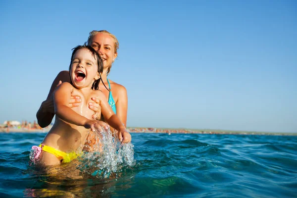 Young mother standing in water and playing with her small daughter — Stock Photo, Image