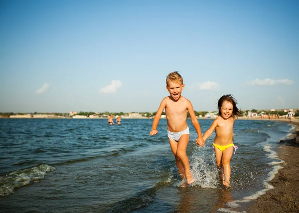 Feliz niña y niño corriendo en el borde del agua bajo el sol —  Fotos de Stock