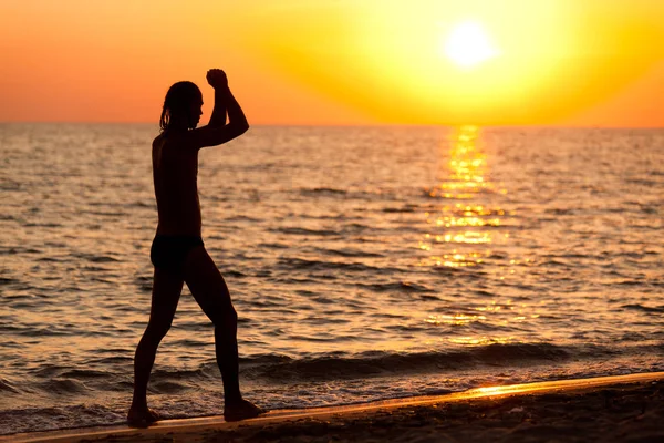 Silhuett av man som rinner på havsvatten kant under gyllene solnedgång — Stockfoto