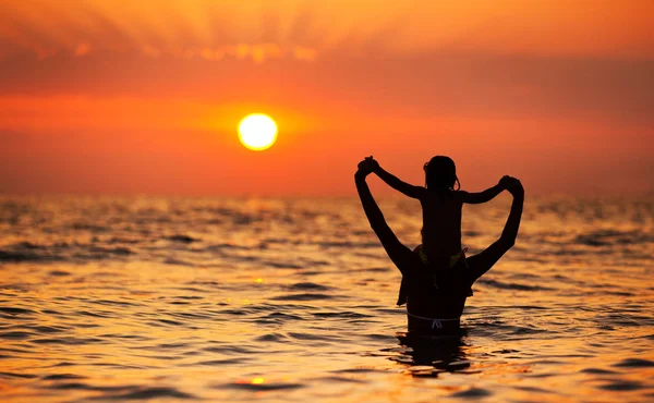 Jovem mãe de pé na água e brincando com sua filha ao pôr do sol — Fotografia de Stock