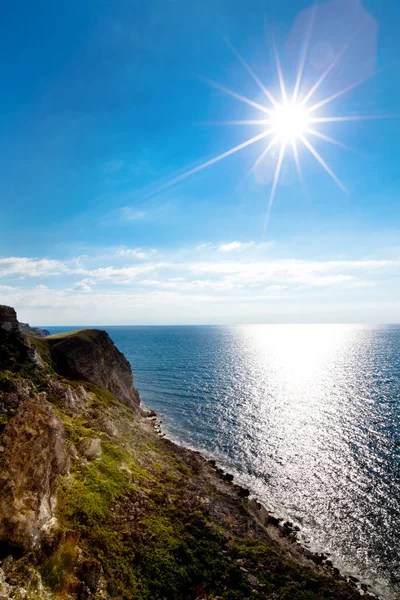 Seascape of still blue sea waters shore, rock coast and bright sun — Stock fotografie
