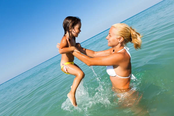 Joven madre de pie en agua azul y jugando con su hija sonriente — Foto de Stock