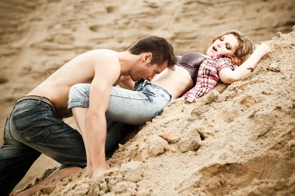 Joven hombre en jeans besándolo novia en suelo arenoso en el día de verano — Foto de Stock