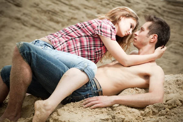Kot pantolonlu genç bir kadın yaz günü kumlu zeminde erkek arkadaşının üzerinde oturuyor. — Stok fotoğraf
