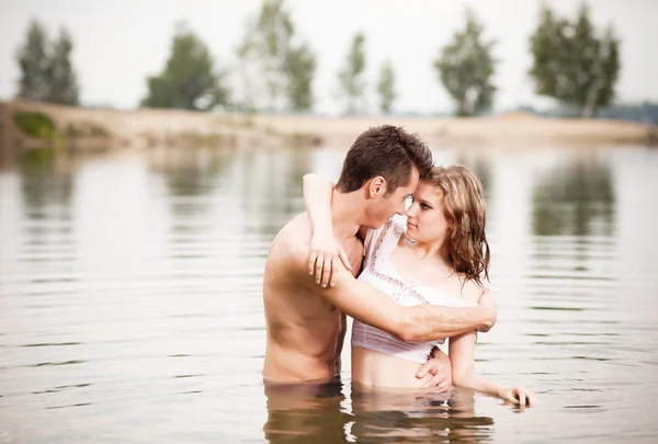 Νεαρό όμορφο ζευγάρι στέκεται σε ήρεμο νερό και κοιτάζονται την καλοκαιρινή μέρα — Φωτογραφία Αρχείου