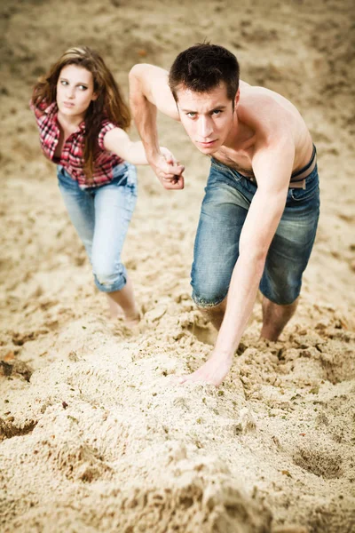 Jeune homme tenant sa copine à la main et montant sur une colline sablonneuse — Photo