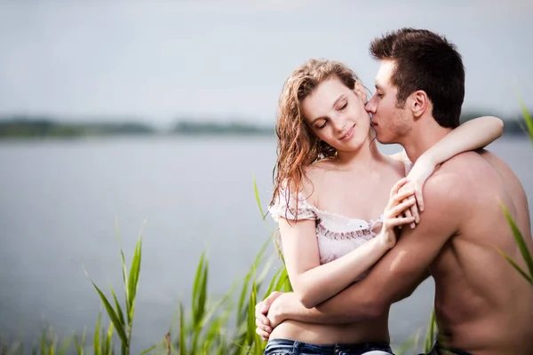Young beautiful loving couple having rest on river shore on summer day with green nature at background — 스톡 사진