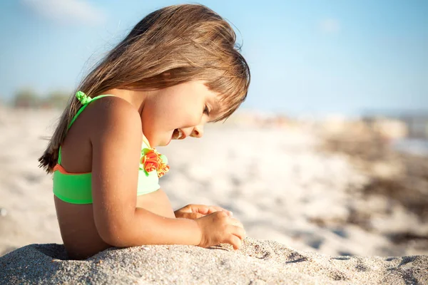 Niña sentada y jugando con arena en la playa —  Fotos de Stock