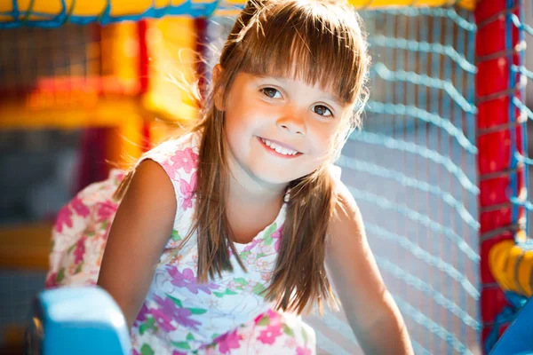 Маленька усміхнена дівчинка в сукні, сидячи в барвистих м'яких декоративних кулях в ігровій кімнаті — стокове фото