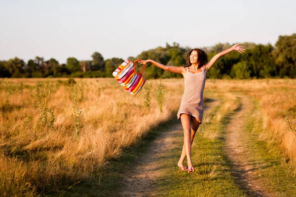 Jong sexy brunette vrouw in mini jurk met zak springen op het platteland weg en het gevoel gelukkig op zomerdag — Stockfoto