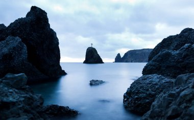 Durgun deniz suları, sert kayalar ve yaz akşamları kayaların zirvesinde kesişen arka planda kasvetli gökyüzü