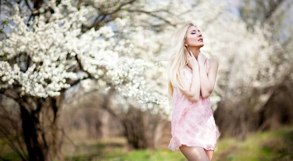 Giovane bella bionda sorridente donna in bianco mini abito in piedi con alberi in fiore sullo sfondo — Foto Stock