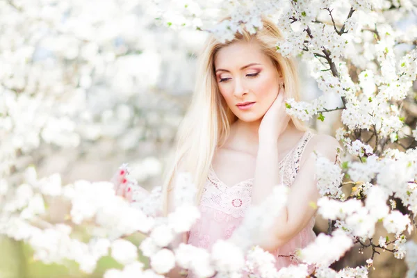 Jong mooi blond glimlachen vrouw in wit mini jurk staan met bloeiende bomen op de achtergrond — Stockfoto