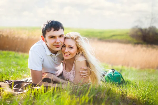 Young beautiful couple woman and man lying on grass and smiling over summer landscape — Stock Photo, Image