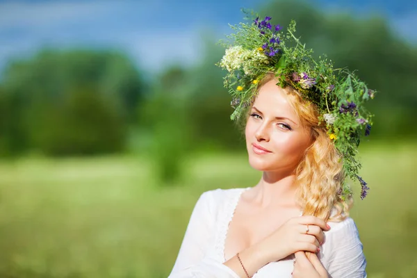 Young beautiful blond woman in white dress and floral wreath standing and looking at camera on summer day — Stock Photo, Image