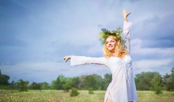 Young beautiful blond woman in white dress and wreath standing with eyes closed and enjoying sunshine on summer day — Stock Photo, Image