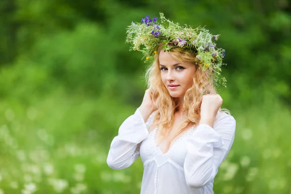 Young beautiful blond woman in white dress and floral wreath standing and smiling on summer day — Stock Photo, Image