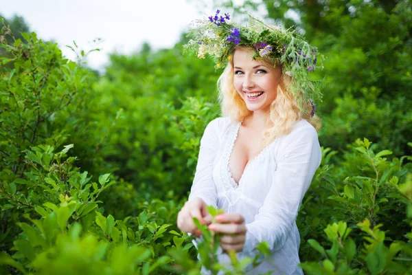 Young beautiful blond woman in white dress and floral wreath standing and smiling on summer day — Stock Photo, Image