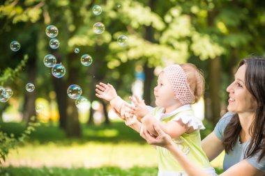 Gülümseyen genç anne küçük kızının kabarcıkları yakalamasına yardım ediyor.