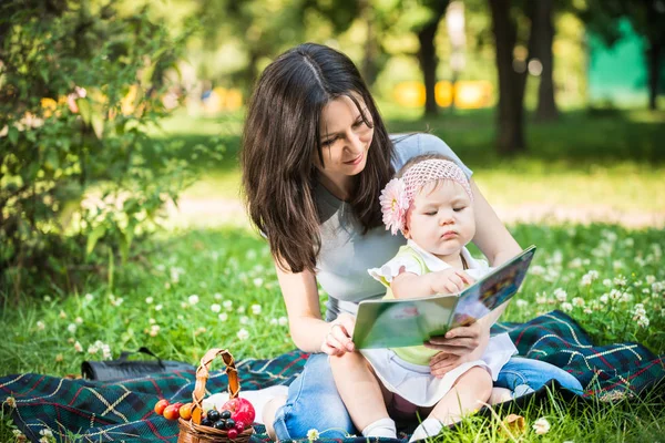 Мати сидить на траві зі своєю маленькою донькою і дивиться на книгу — стокове фото