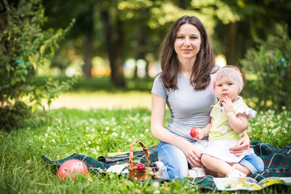 Мати сидить на траві зі своєю маленькою донькою і їсть фрукти — стокове фото