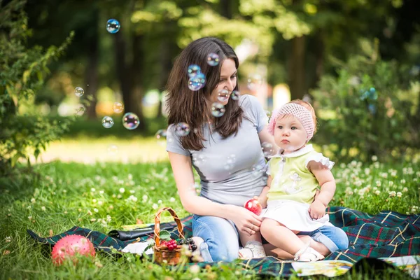 Zâmbind tânără mamă ajutând-o pe fiica ei mică să prindă bule — Fotografie, imagine de stoc