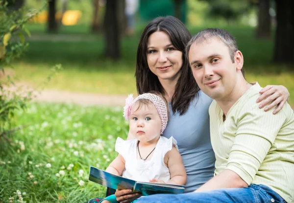 Щасливі батьки сидять у парку зі своєю маленькою донькою на колінах — стокове фото