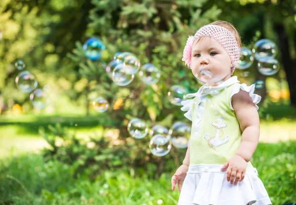 Klein baby meisje in jurk staan en kijken naar bubbels in de lucht — Stockfoto