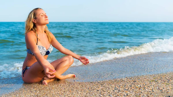Woman in yoga pose sitting by sea — Stock Photo, Image