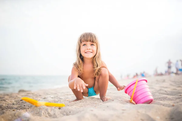 Bambino gioca sulla spiaggia accovacciato nella sabbia — Foto Stock